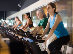 Sporty adult woman doing cardio workout out in female group, training on exercise bike
