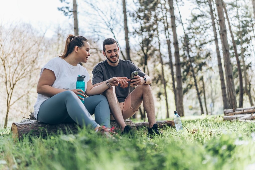 Sitting on a fallen tree trunk, the couple, including the determined overweight female, catch their breath, their laughter blending with the rustling leaves as they enjoy a post-workout moment. Sitting on a fallen tree trunk, the couple, including the determined overweight female, catch their breath, their laughter blending with the rustling leaves as they enjoy a post-workout moment.